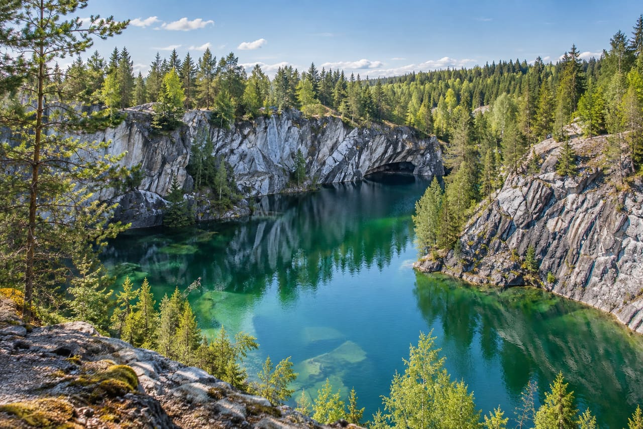 Изумрудная вода мраморного карьера, светло-серые скалы и сосновый лес