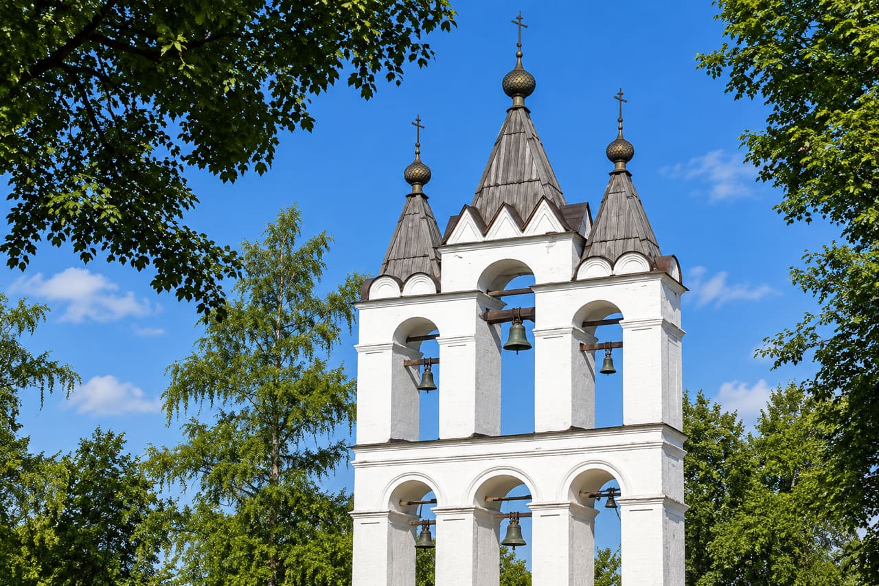 Белая трёхпролётная звонница Больших Вязём среди деревьев