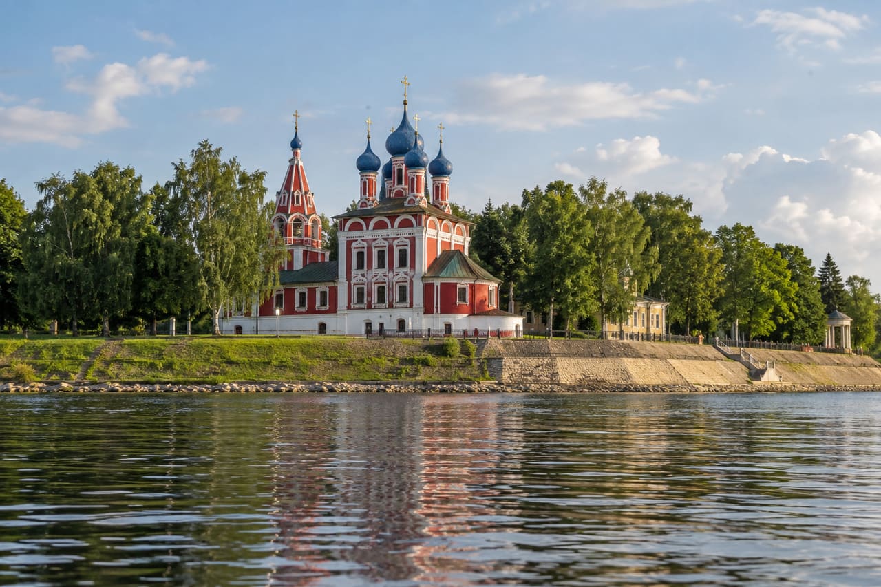 Красная церковь с синими куполами на берегу широкой реки